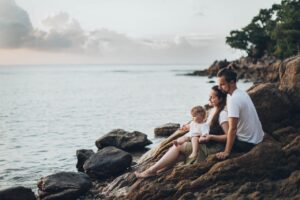 mother husband and child sitting on a rocky shore by beach