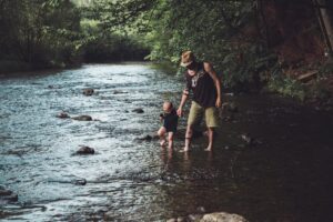 father standing with baby in a shallow river