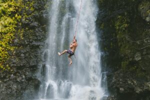 man swinging on a rope by a waterfall