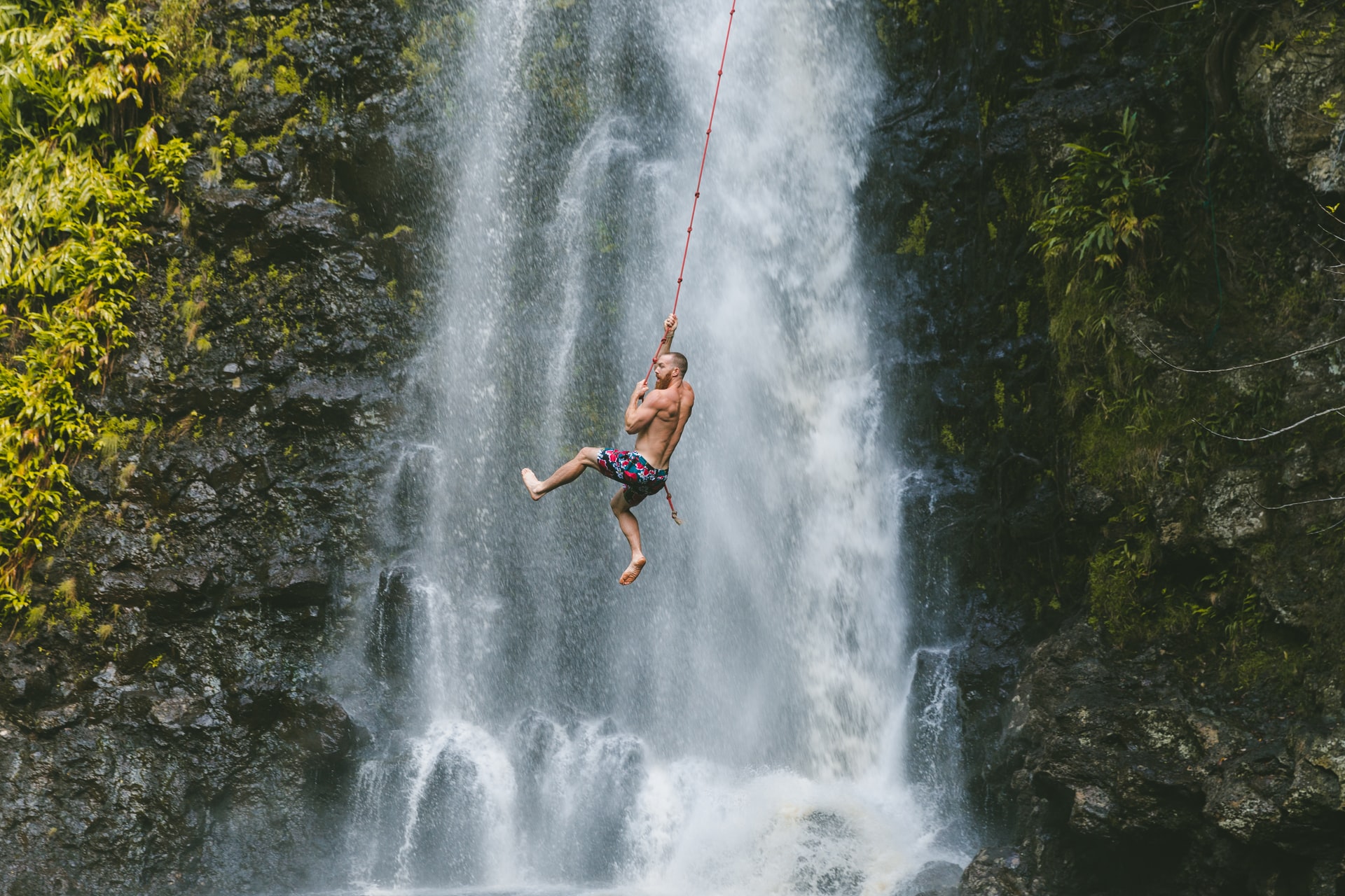 man swinging on a rope by a waterfall