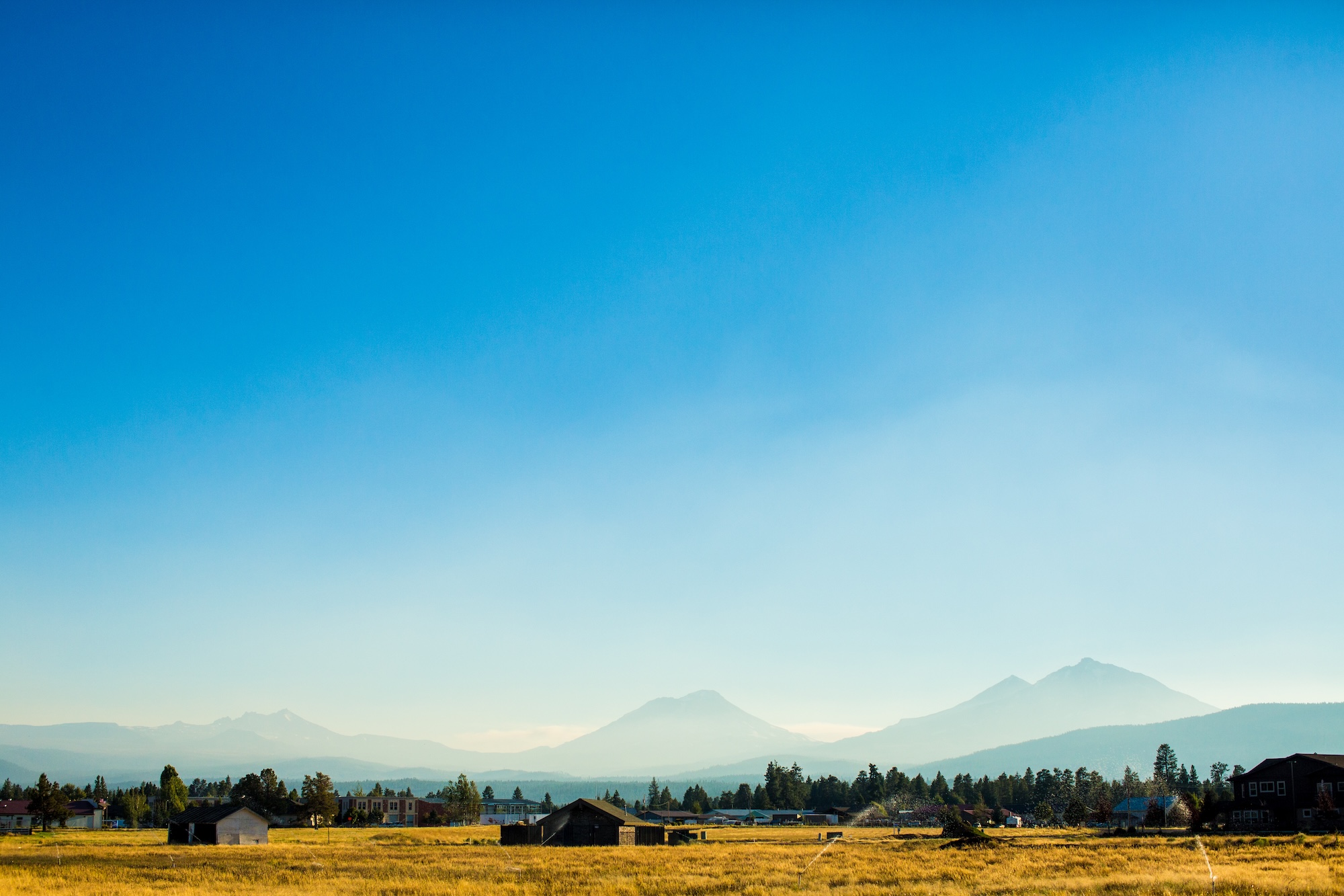 On a sunny evening, the Three Sisters Mountains rise above farmland in the town of Sisters, OR.
